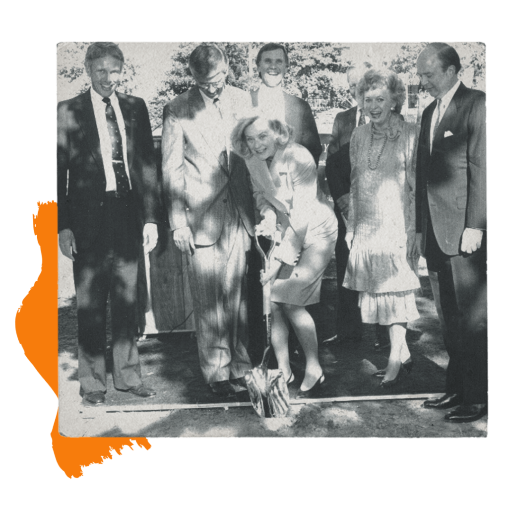 A group of people standing around a lading with a shovel at a breaking ground ceremony