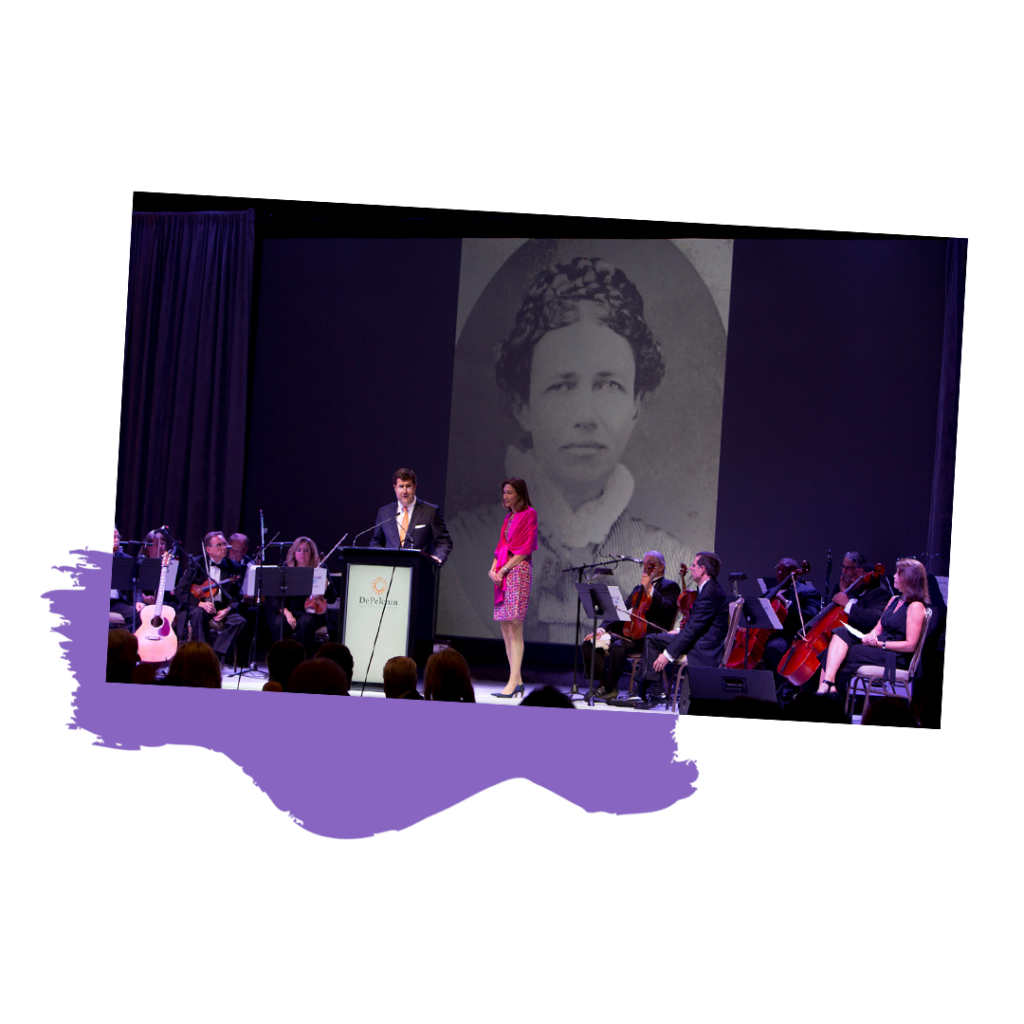 A man speaking at a podium with an orchestra behind him