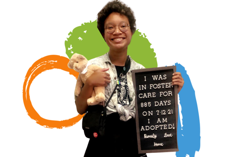 A teenager hold a sign that says, I was in foster care for 885 days on 7-12-21. I am adopted!