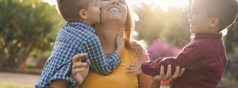 A lady being hugged and kissed by two little boys